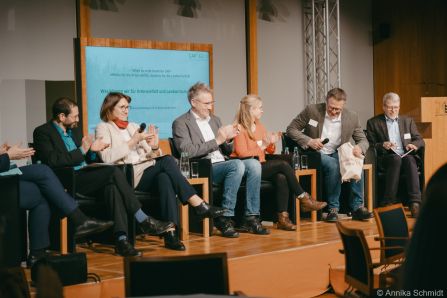 Teilnehmende der Podiumsdiskussion klatschen, während sich Jürgen Schell setzt
